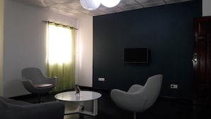 Una habitación moderna con dos sillas, una mesita, un televisor de pantalla plana en la pared y una ventana con cortinas.
