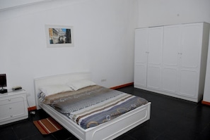 A bedroom with a bed, a nightstand, a wardrobe, and a framed picture on the wall. - Apartamentos Santiago (Praia)