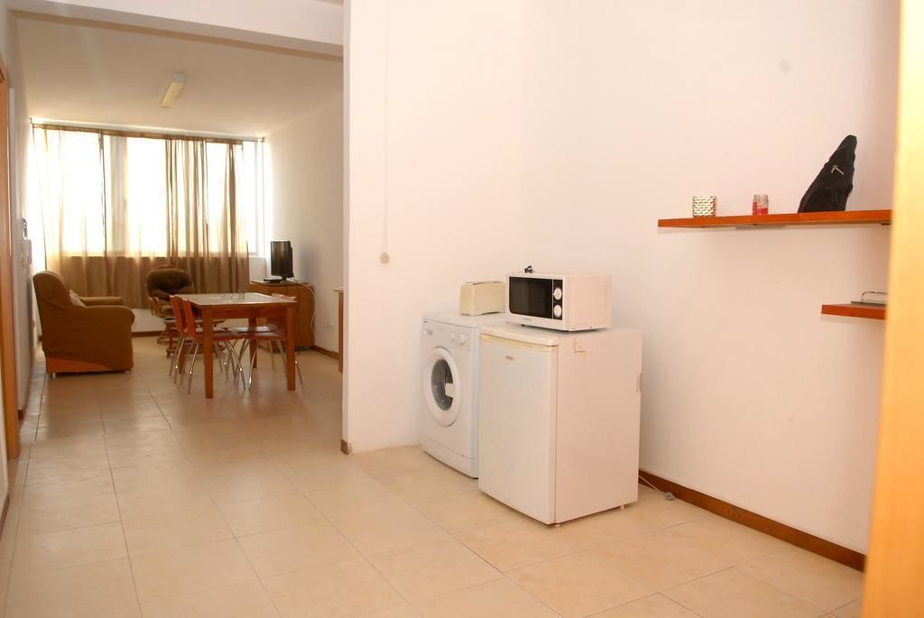 A compact living space with a washing machine, a microwave, a dining area with a table and chairs, and a sofa.