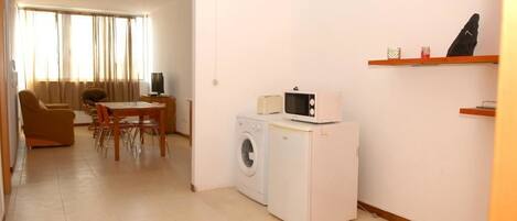 A compact living space with a washing machine, a microwave, a dining area with a table and chairs, and a sofa.