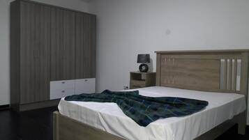Ein Schlafzimmer mit einem Bett, einem Kleiderschrank, einem Nachttisch mit Lampe und einer Wandsteckdose.