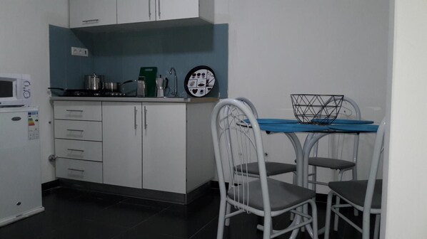 A compact kitchen with white cabinets, a microwave, a coffee maker, and a wall clock.