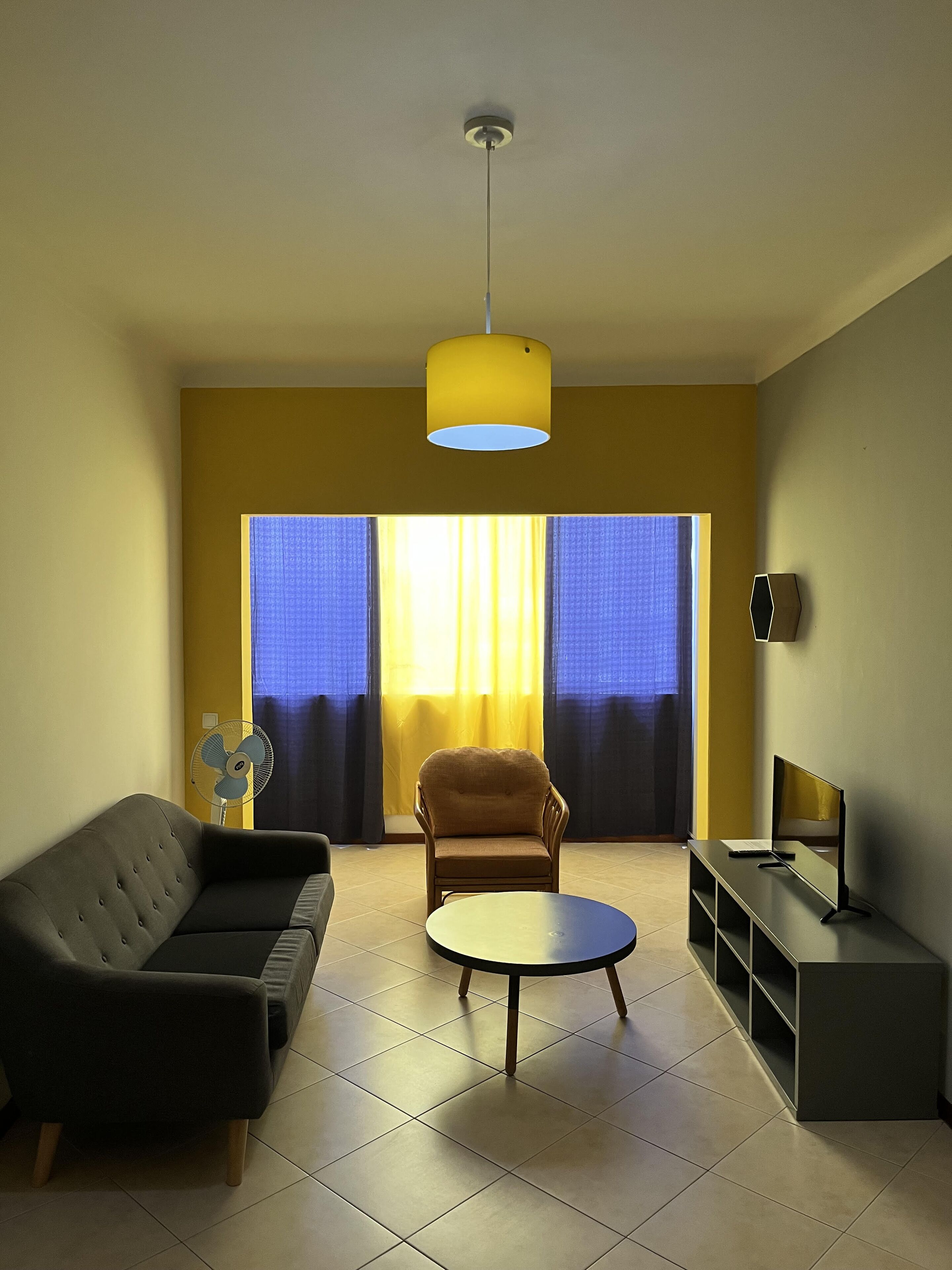 A modern living room with a sofa, armchair, round coffee table, and a TV stand.