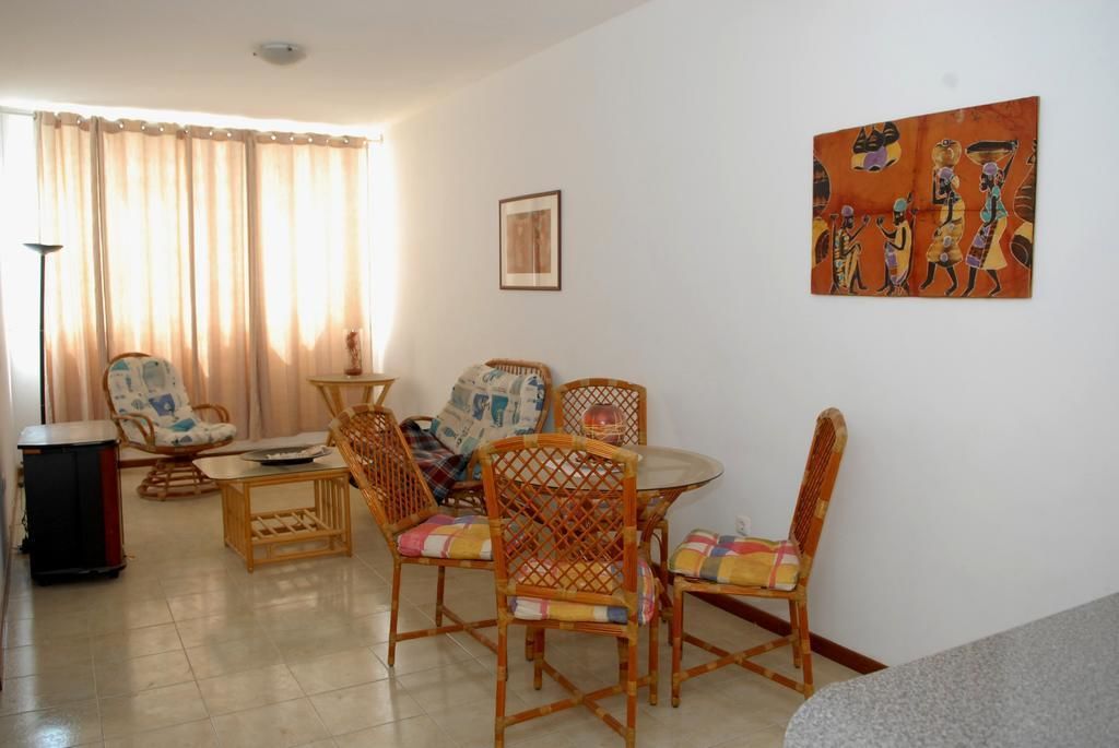 A living room with a dining table, wicker chairs, a sofa, and a painting on the wall.