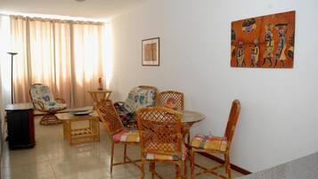 A living room with a dining table, wicker chairs, a sofa, and a painting on the wall.