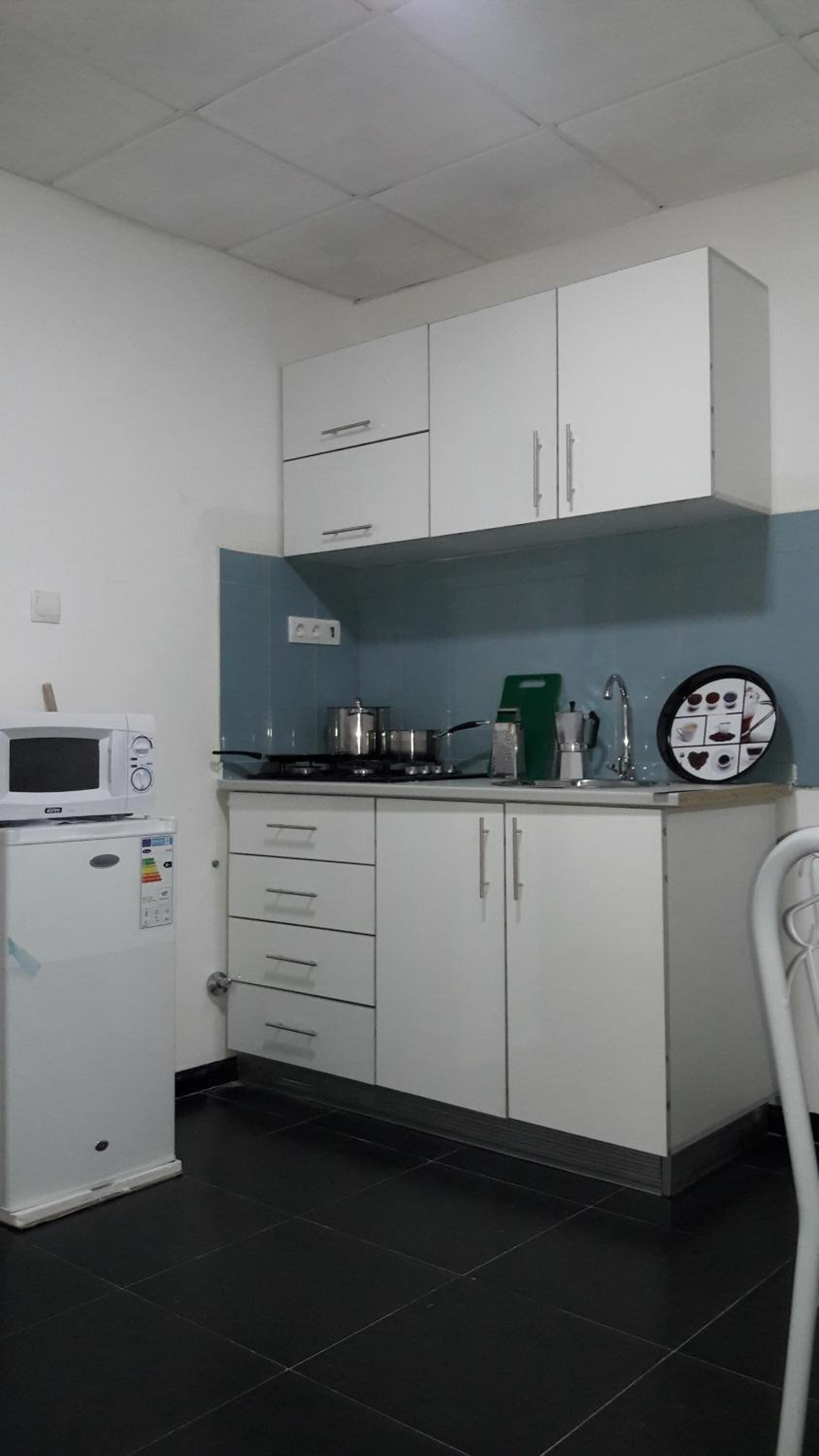 Una cocina compacta con armarios blancos, un microondas, una estufa y una cafetera.