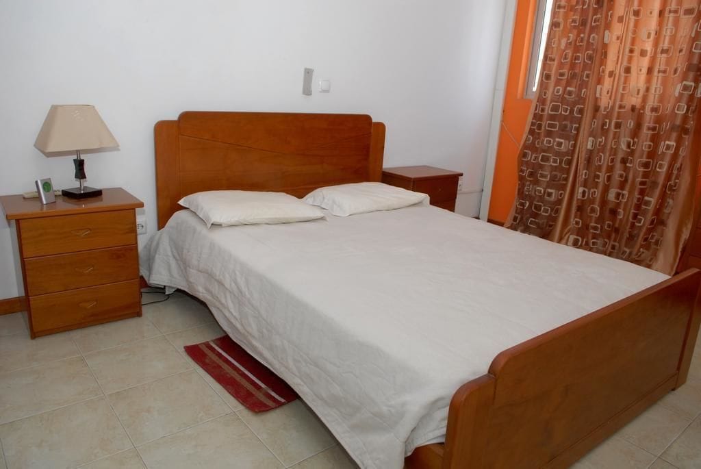 A bedroom with a wooden bed, a nightstand with a lamp, and a red rug.