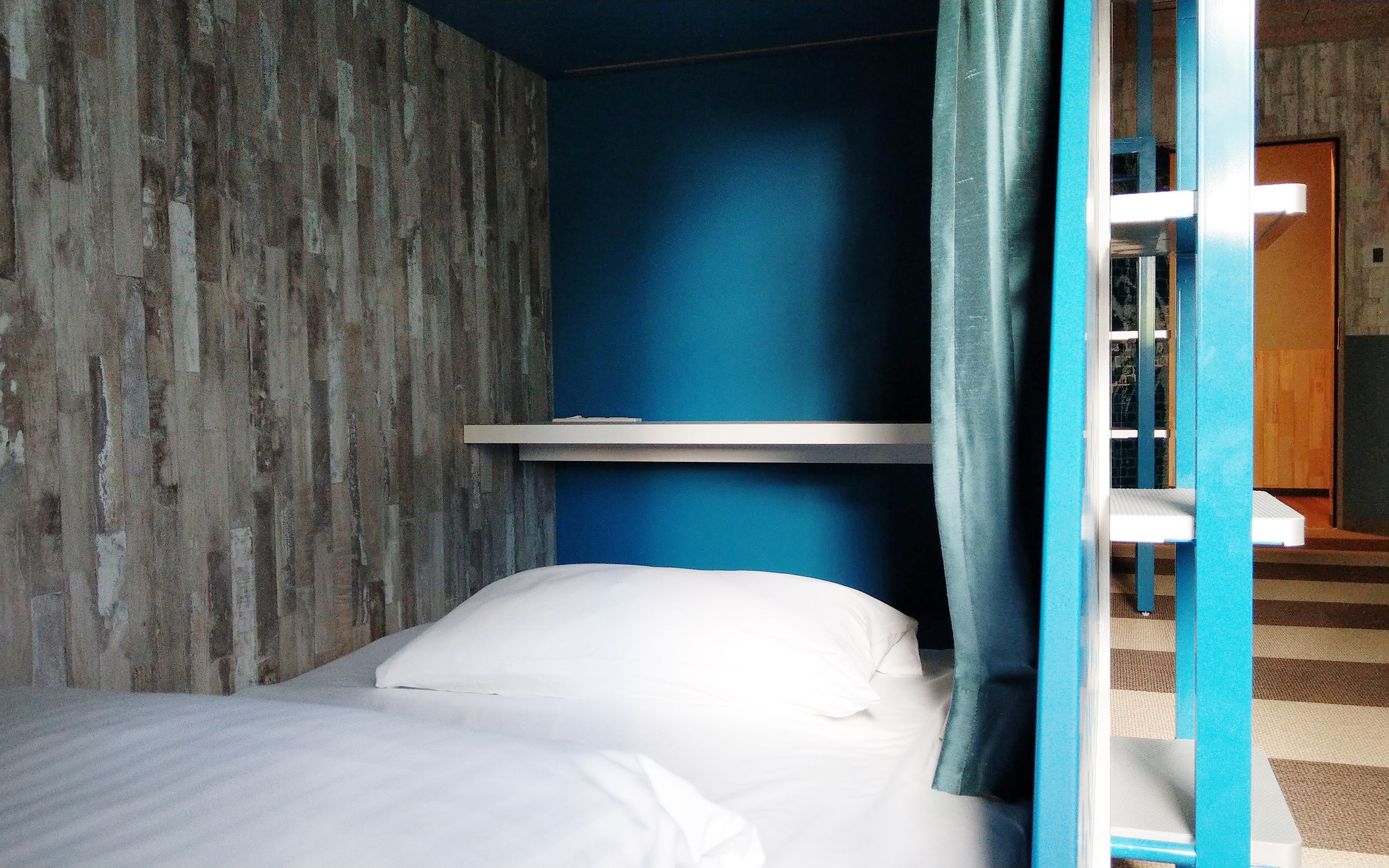 Een eenpersoonsbed met witte lakens in een kamer met blauwe wanden en een wand met een houtstructuur aan één kant.