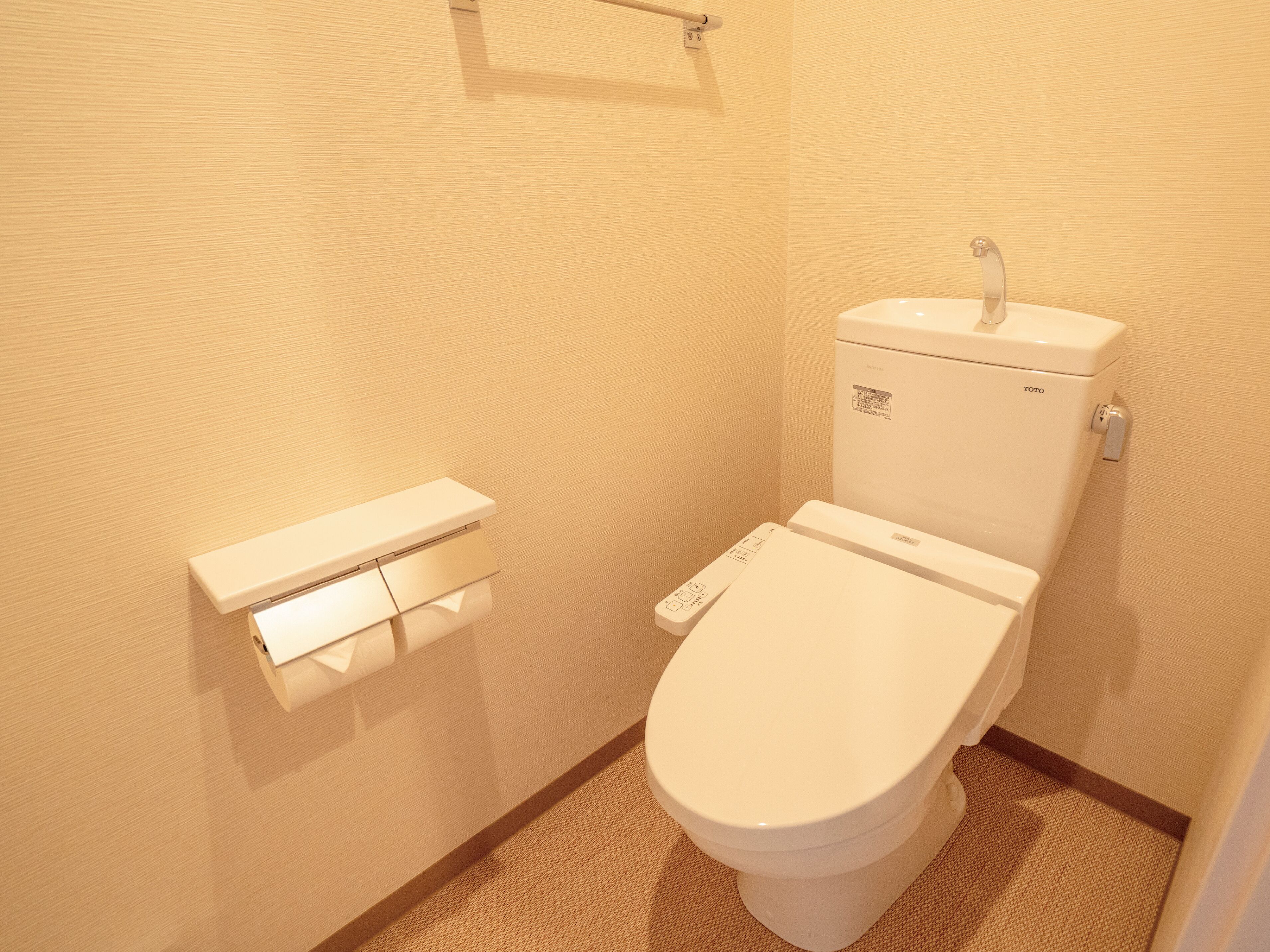 Un baño moderno y funcional con un inodoro blanco, un dispensador de papel higiénico y tanque de inodoro TOTO.