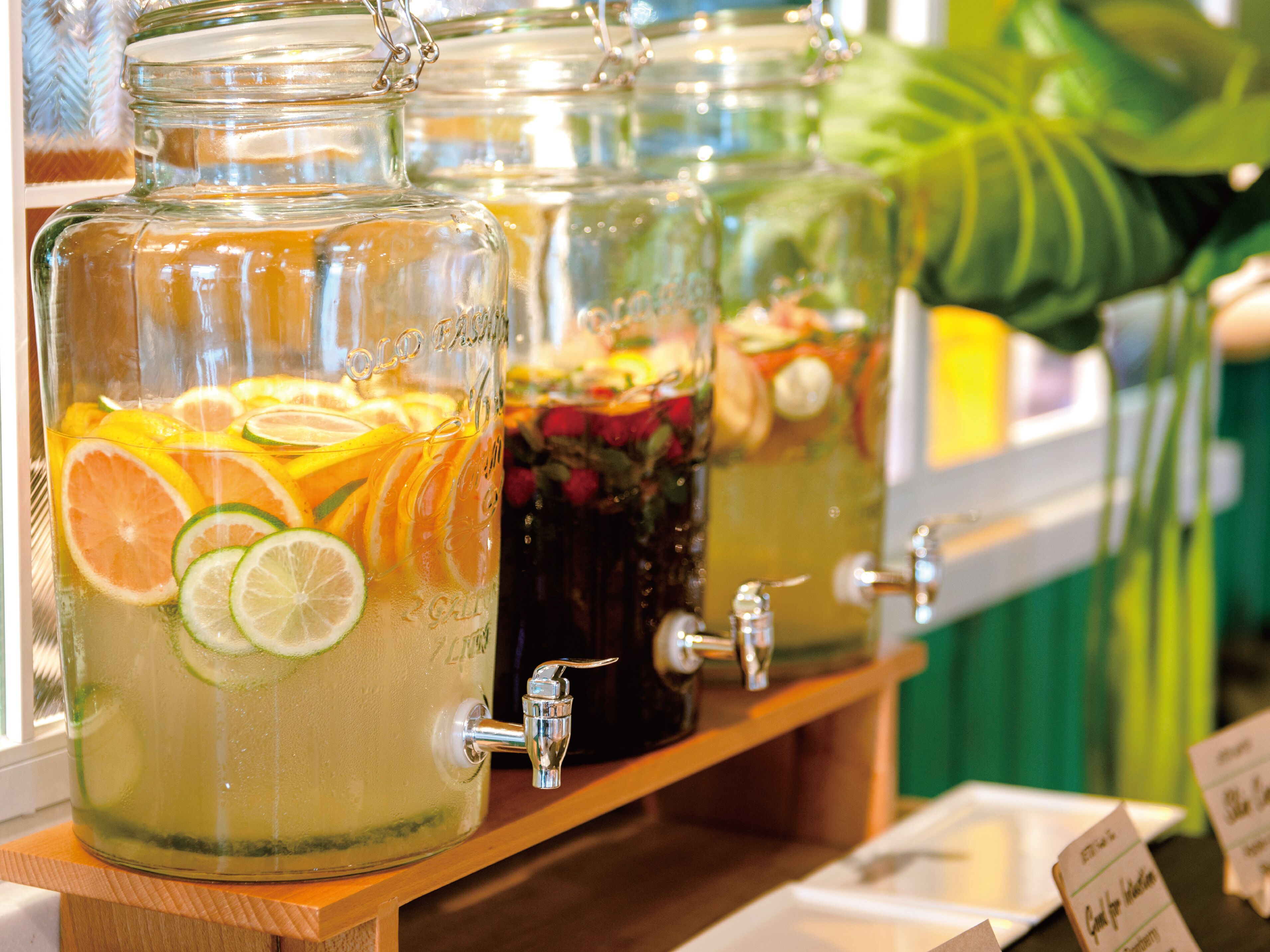 Une rangée de bocaux en verre contenant des tranches de fruits et dotés d’un robinet, probablement destinés à un distributeur de boissons.