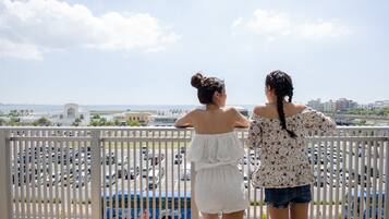Zwei Frauen stehen auf einem Balkon mit Blick auf einen Parkplatz und eine entfernte Skyline.