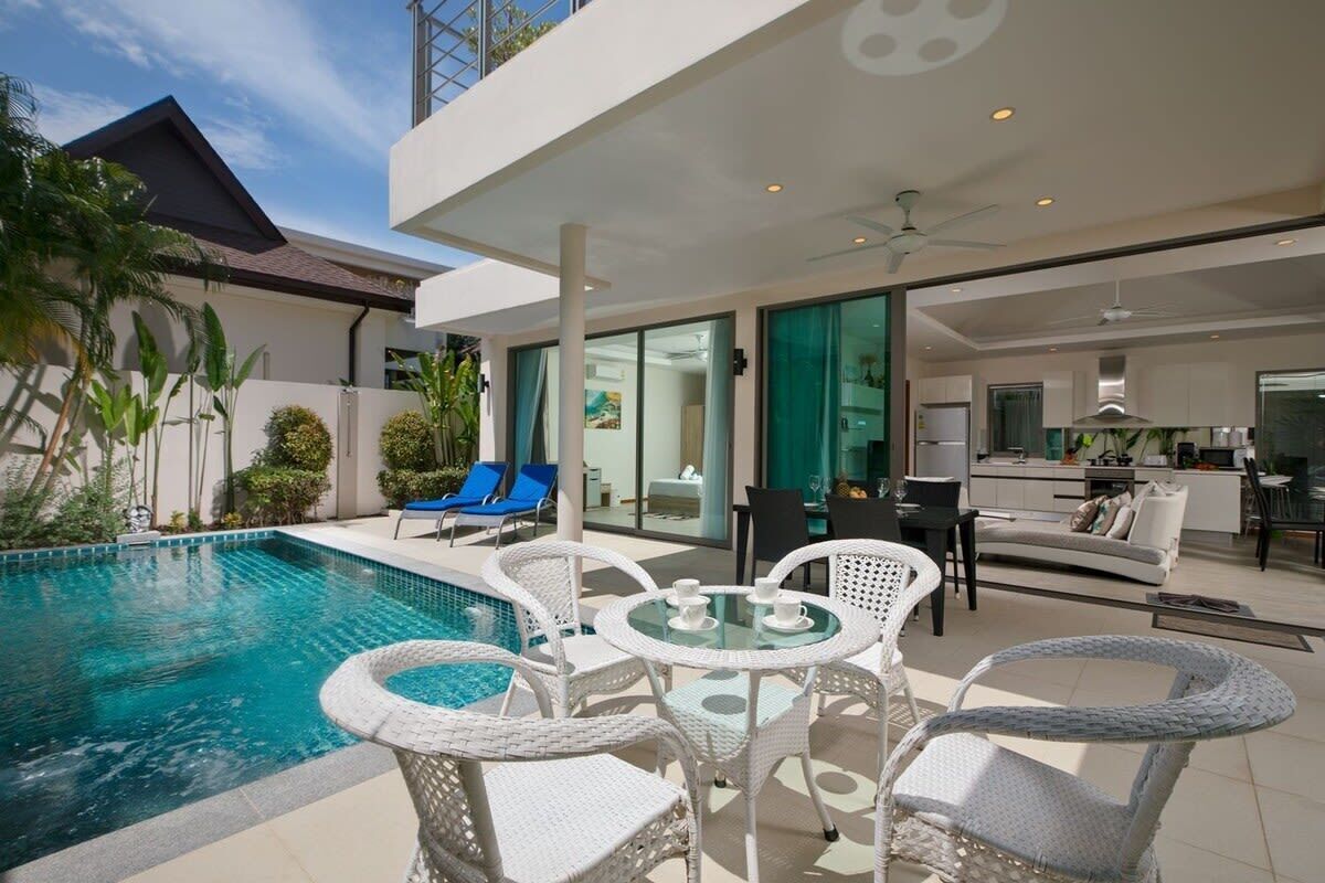 Una casa moderna con piscina, mobiliario exterior y una cocina visible a través de puertas de vidrio.