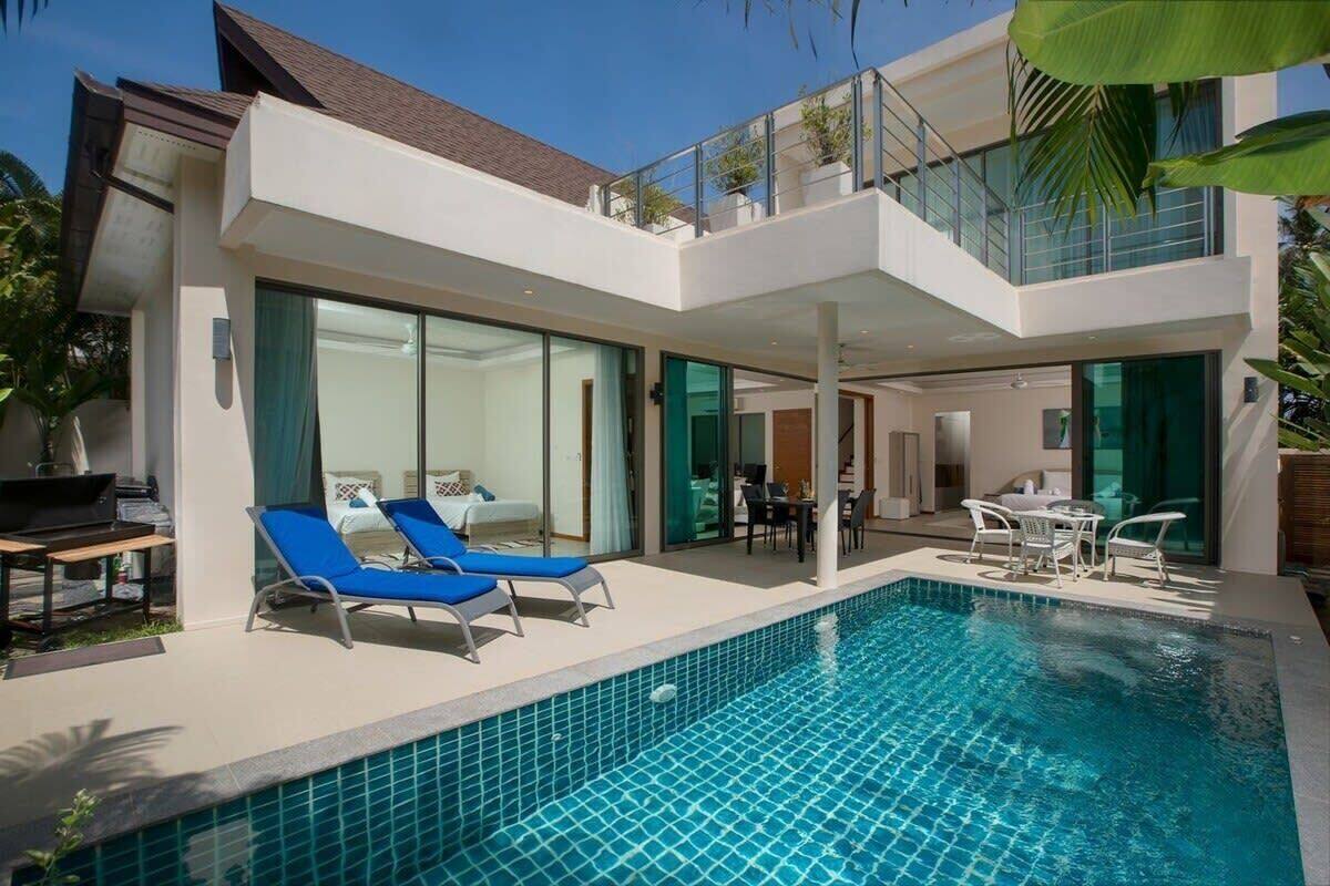 Une maison moderne à deux étages, dotée d’une piscine, de chaises longues et d’un coin repas.