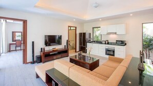 Een moderne woonkamer met een bank, salontafel, televisie en keukenhoek.