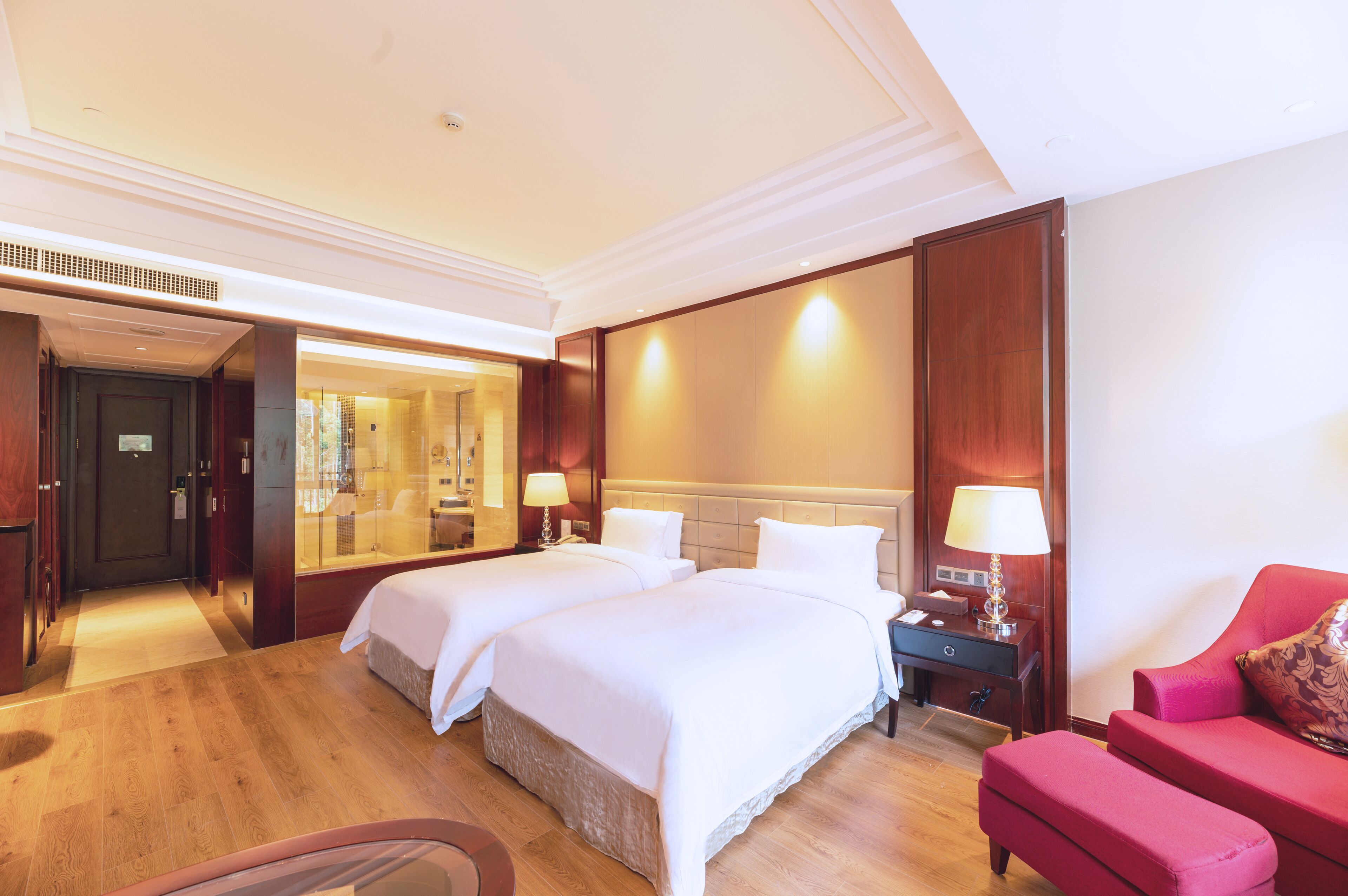 A hotel room with two beds, a red sofa, a desk with a lamp, and a mirror.