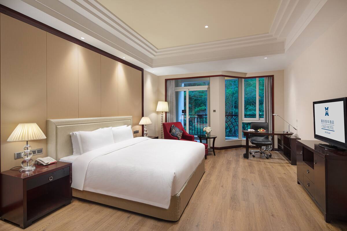 A hotel room with a large bed, bedside tables, a desk, a chair, and a TV.