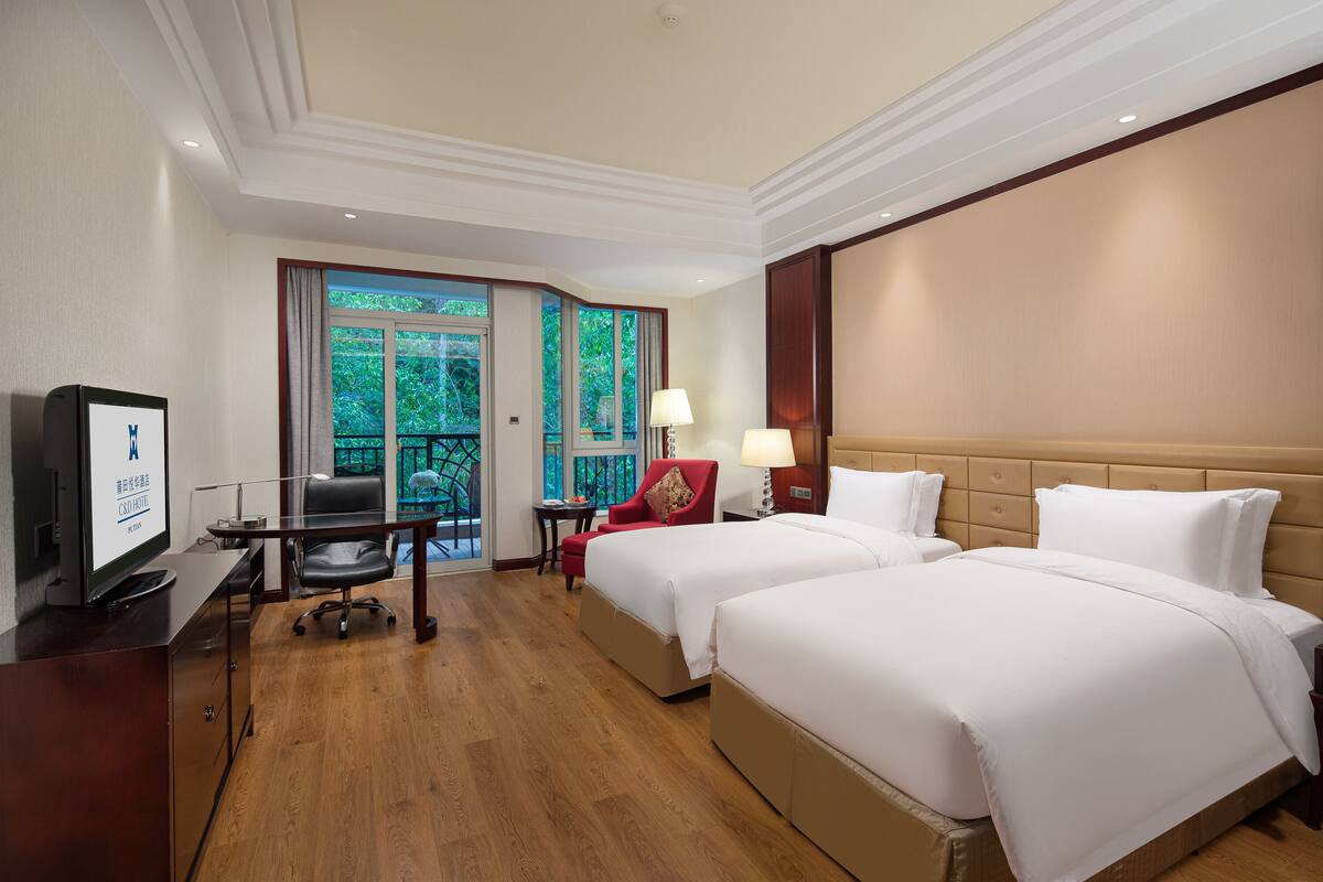 A hotel room with two beds, a desk with a computer, a chair, and a TV.