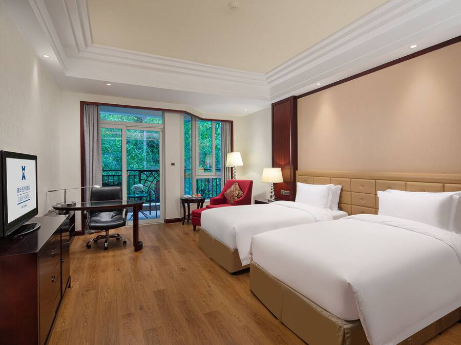 A hotel room with two beds, a desk with a computer, a chair, and a TV.