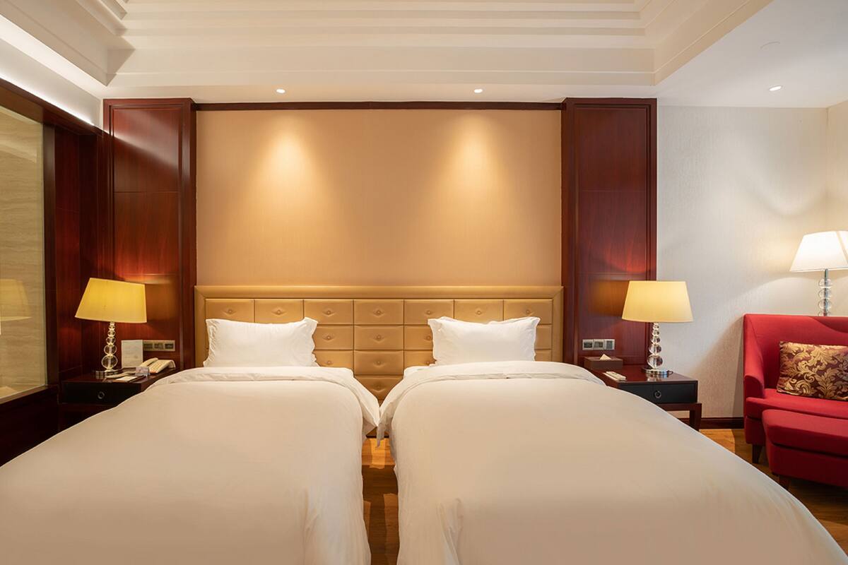 A hotel room with two beds, a red armchair, and a large mirror.