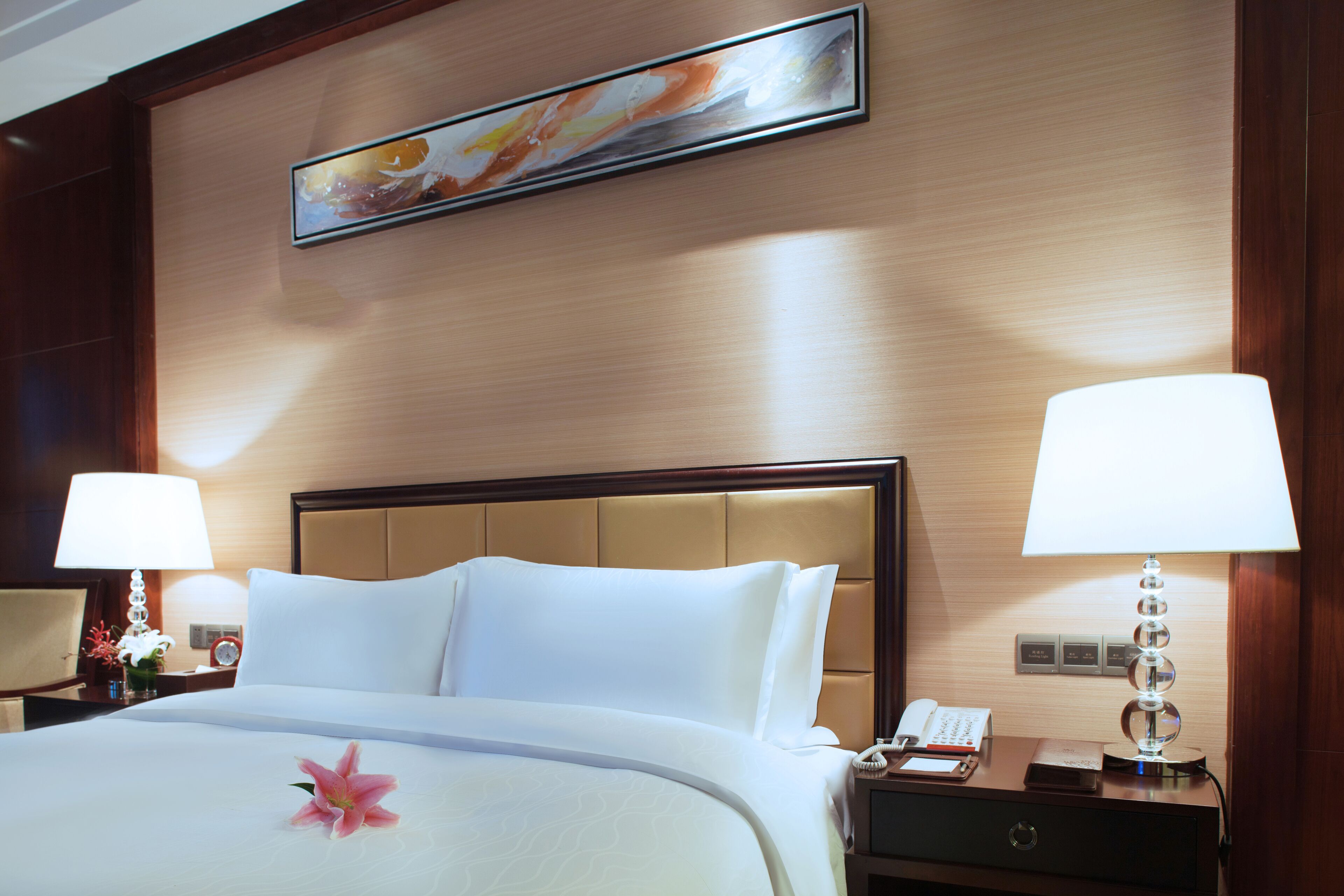 Habitación de hotel con una cama grande, dos lámparas de noche, una mesita de noche con un teléfono y una lámpara, y un cuadro en la pared.