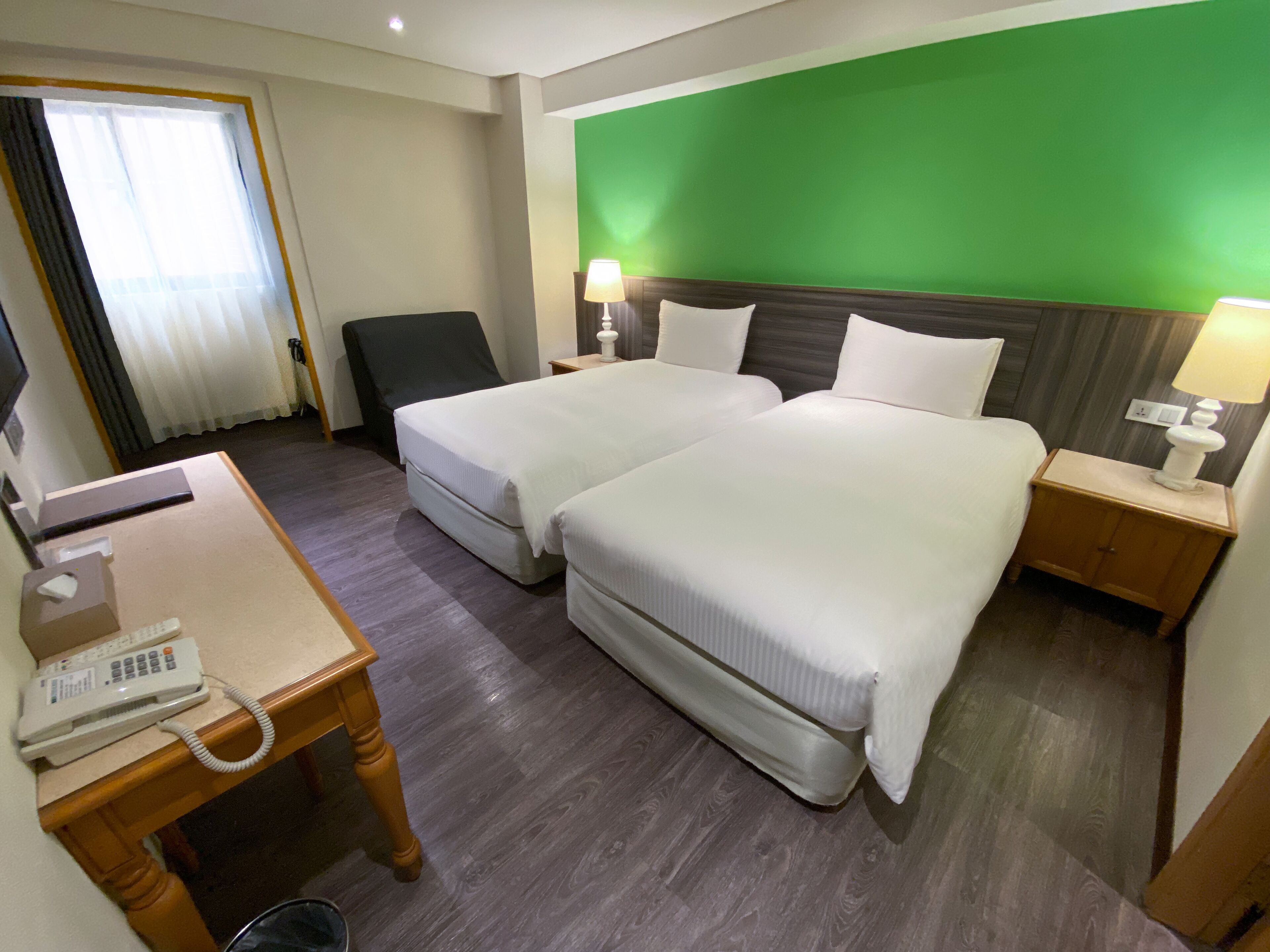 Ein Hotelzimmer mit zwei Betten, einem Schreibtisch mit Telefon und einer grünen Wand.