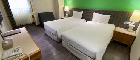 Ein Hotelzimmer mit zwei Betten, einem Schreibtisch mit Telefon und einer grünen Wand.