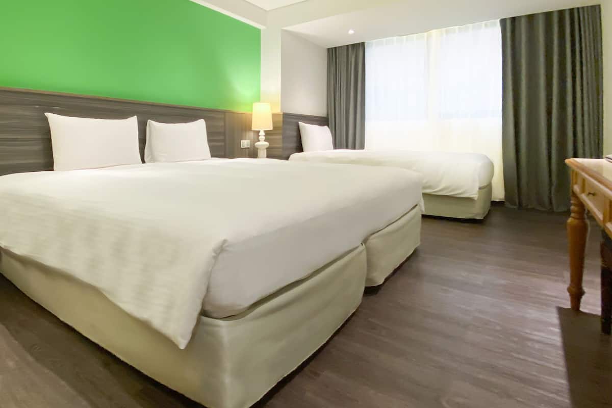 A hotel room with two beds, a green wall, a window with curtains, and a wooden nightstand.