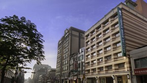 Een meerhoog hotel met een gestreepte gevel, meerdere balkons en een bord dat aangeeft dat het een hotel met driepersoonskamers is.