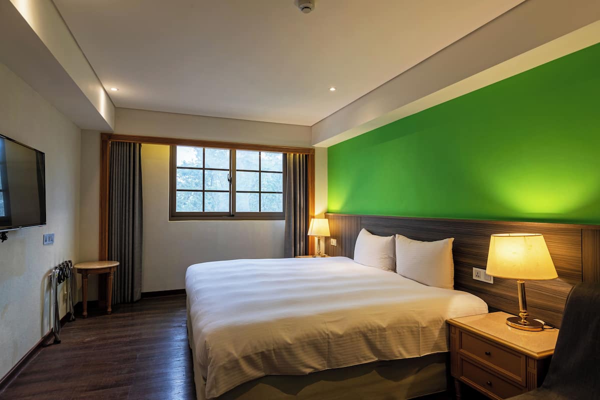 A hotel room with a large bed, bedside tables, a TV, and a window with curtains.