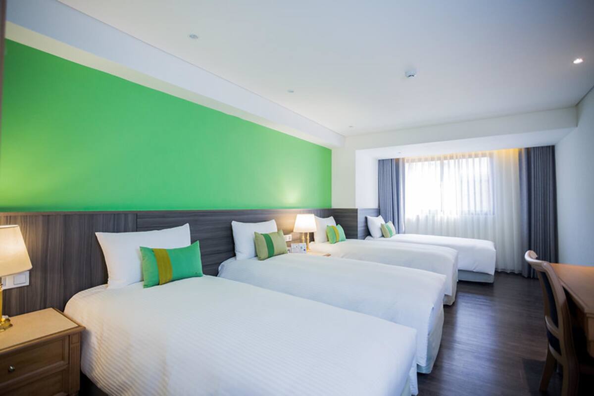 A hotel room with three beds, a desk, and a window with curtains.