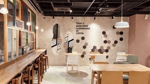 Een modern café-interieur met houten tafels en stoelen, een grote wandklok en zeshoekige decoratie aan de muur.