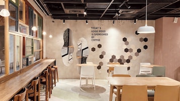 Interior moderno de café com mesas e cadeiras de madeira, um grande relógio de parede e arte de parede hexagonal.