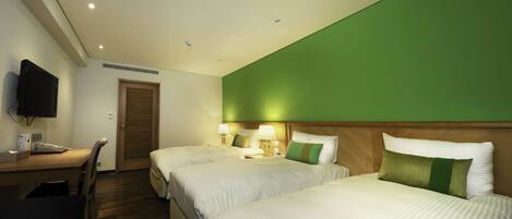 A hotel room with two beds, a desk, a television, and a green accent wall.