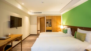 Een hotelkamer met twee bedden, een aan de muur bevestigde televisie, een houten bureau en een groene accentmuur.