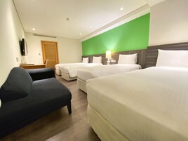 Een hotelkamer met drie bedden, een bureau, een stoel en een groene accentmuur.