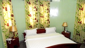 A neatly made bed with white linens, two bedside tables with lamps, and floral curtains. - Hotel Magnificat Baguida (Lomé)