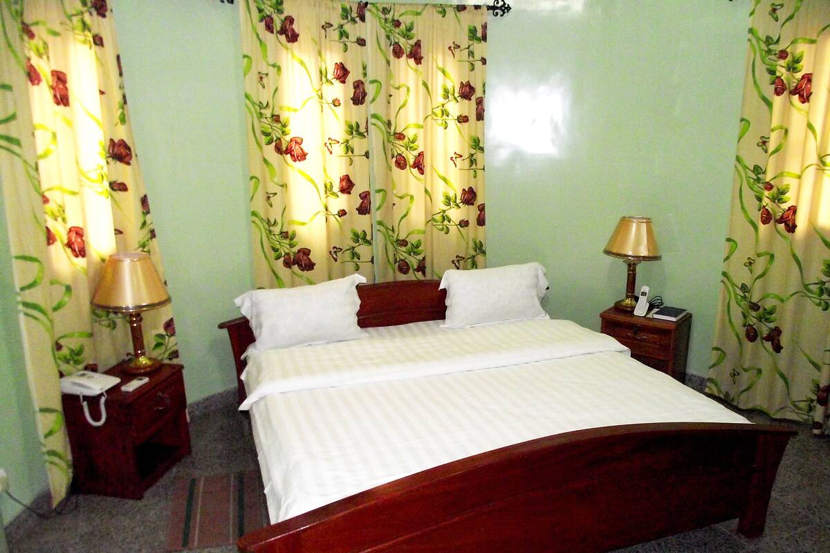 A neatly made bed with white linens, two bedside tables with lamps, and floral curtains.