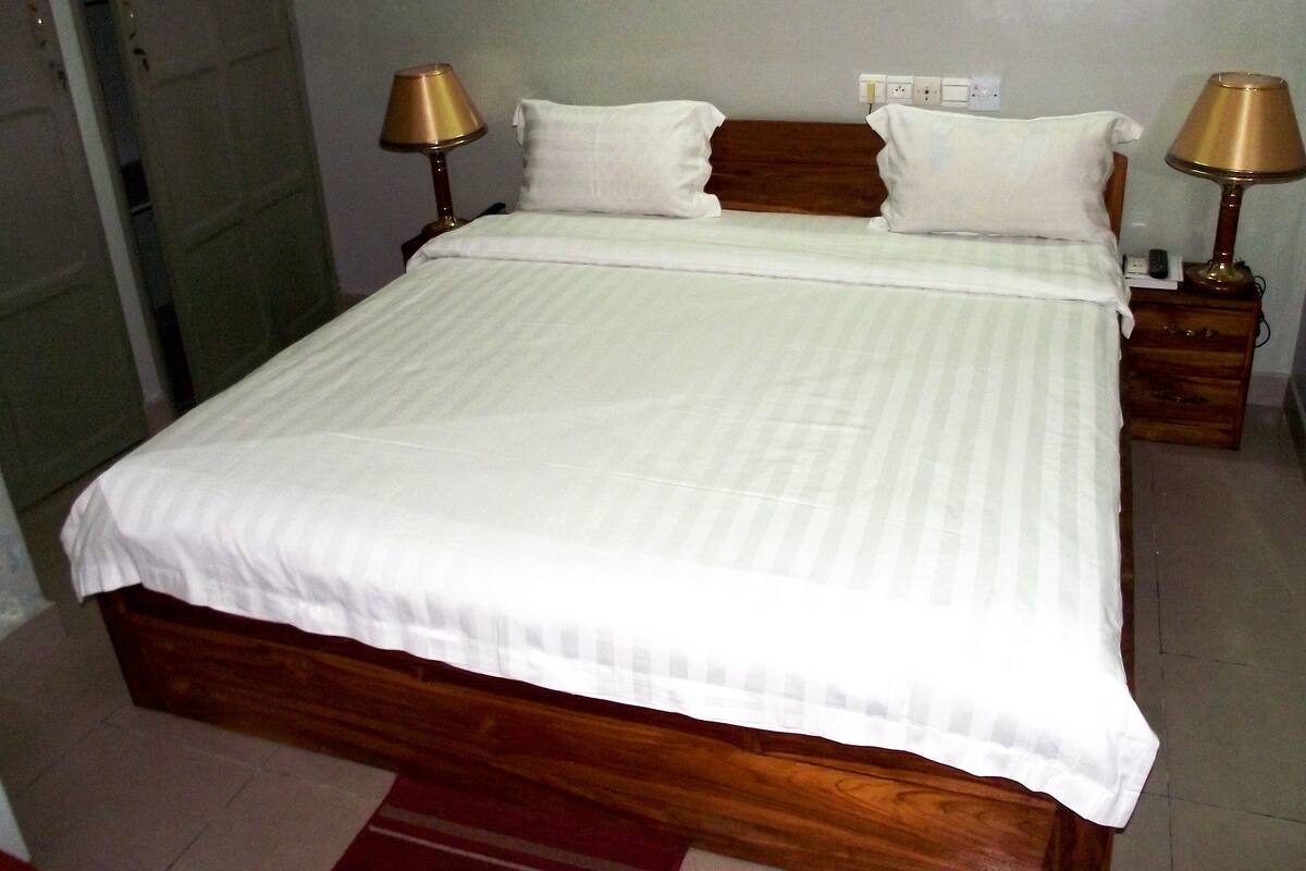 A neatly made bed with white linens, two bedside lamps, and a wooden headboard.