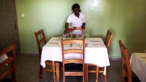 A dining area with a table set for two, a waiter, and a painting on the wall. - Hotel Magnificat Baguida (Lomé)