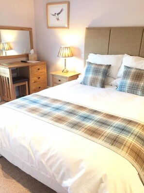 A neatly made bed with a plaid bedspread, a bedside lamp, a wooden desk with drawers, and a framed picture on the wall. - The Drayton Crown (Langport)