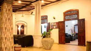 A lobby with a stone column, a large vase, and a wooden door with intricate carvings. - Shanthi beach resort (Unawatuna)