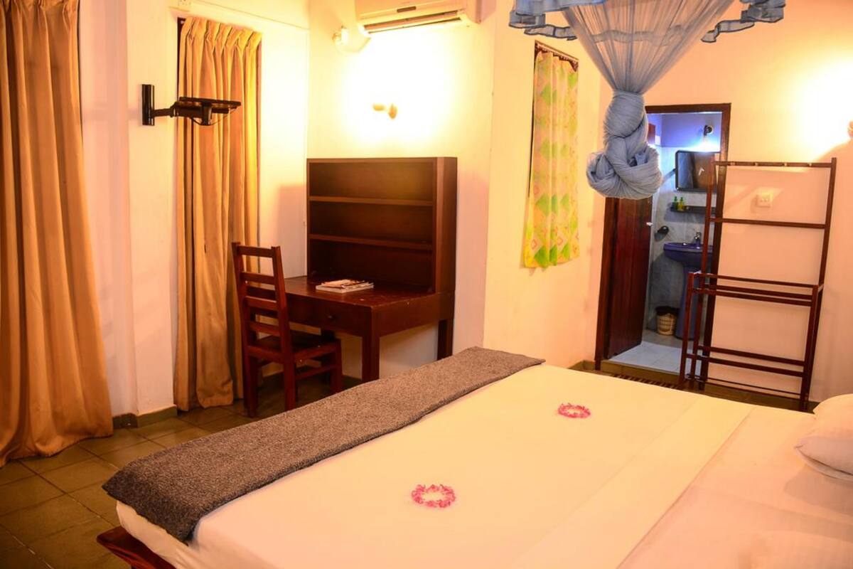A hotel room with a bed, a desk, a chair, a wardrobe, and a bathroom visible through an open door.