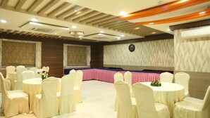 A conference room with round tables and chairs, a stage, and a patterned wall. - Moments (Lucknow)