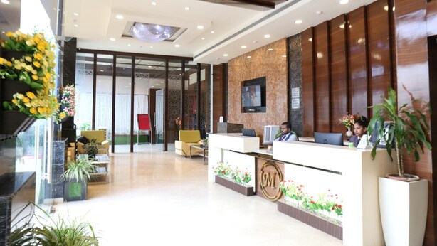 A hotel reception area with a modern design, featuring a reception desk, seating area, and a large window providing natural light. - Moments (Lucknow)