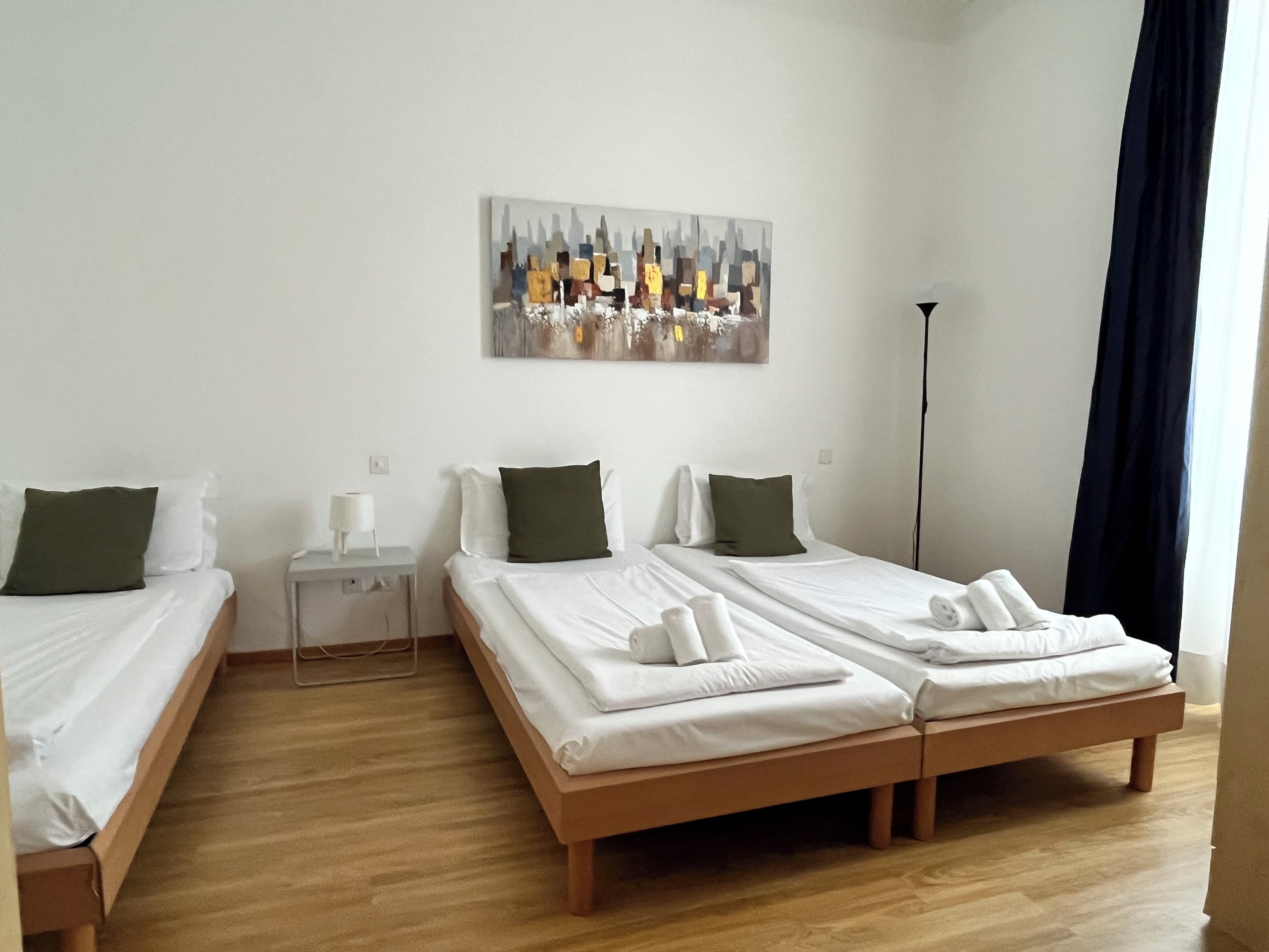 A hotel room with two single beds, a nightstand, a lamp, and a painting on the wall.