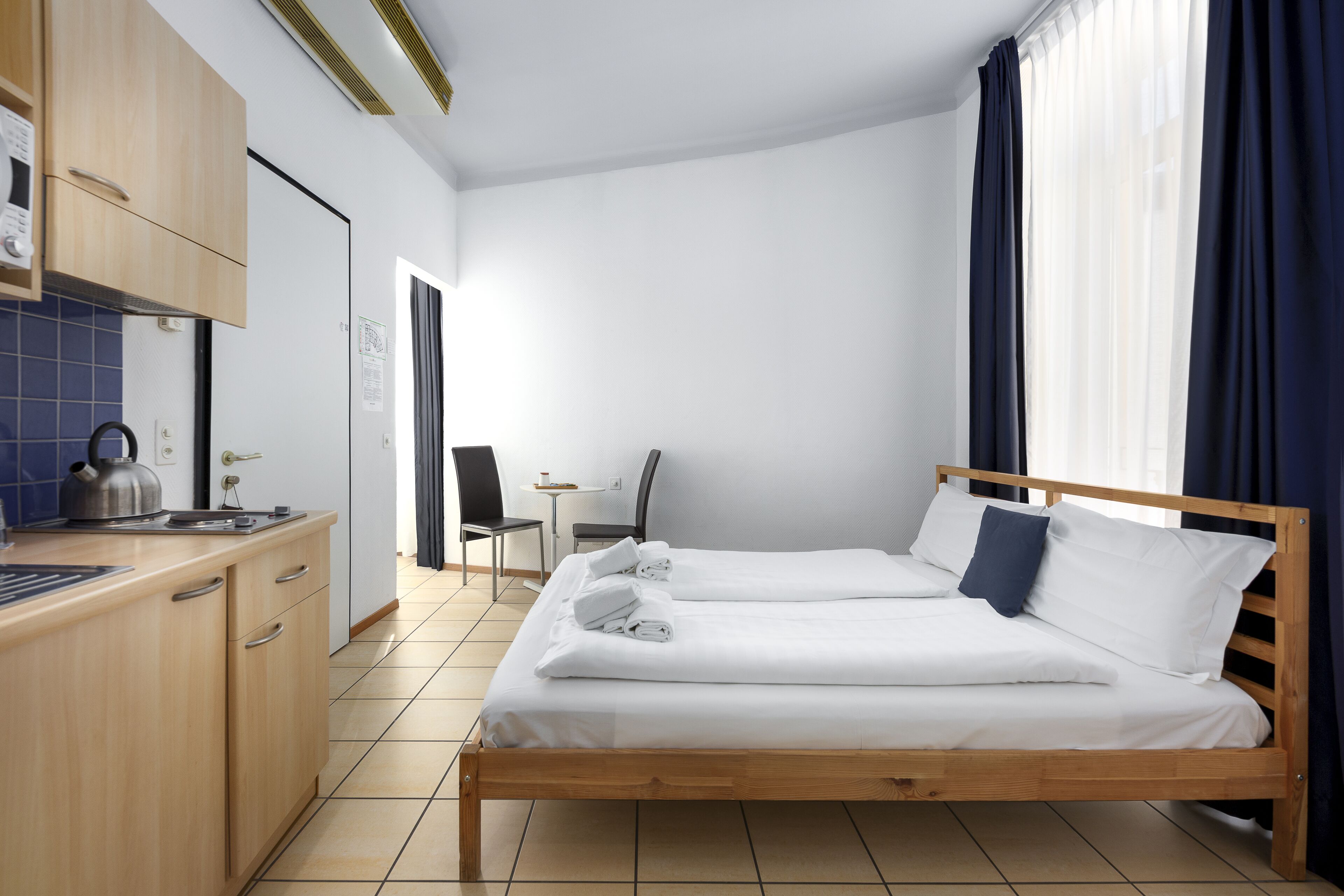 Une chambre d’hôtel avec un lit en bois, une petite kitchenette, un bureau et une chaise.