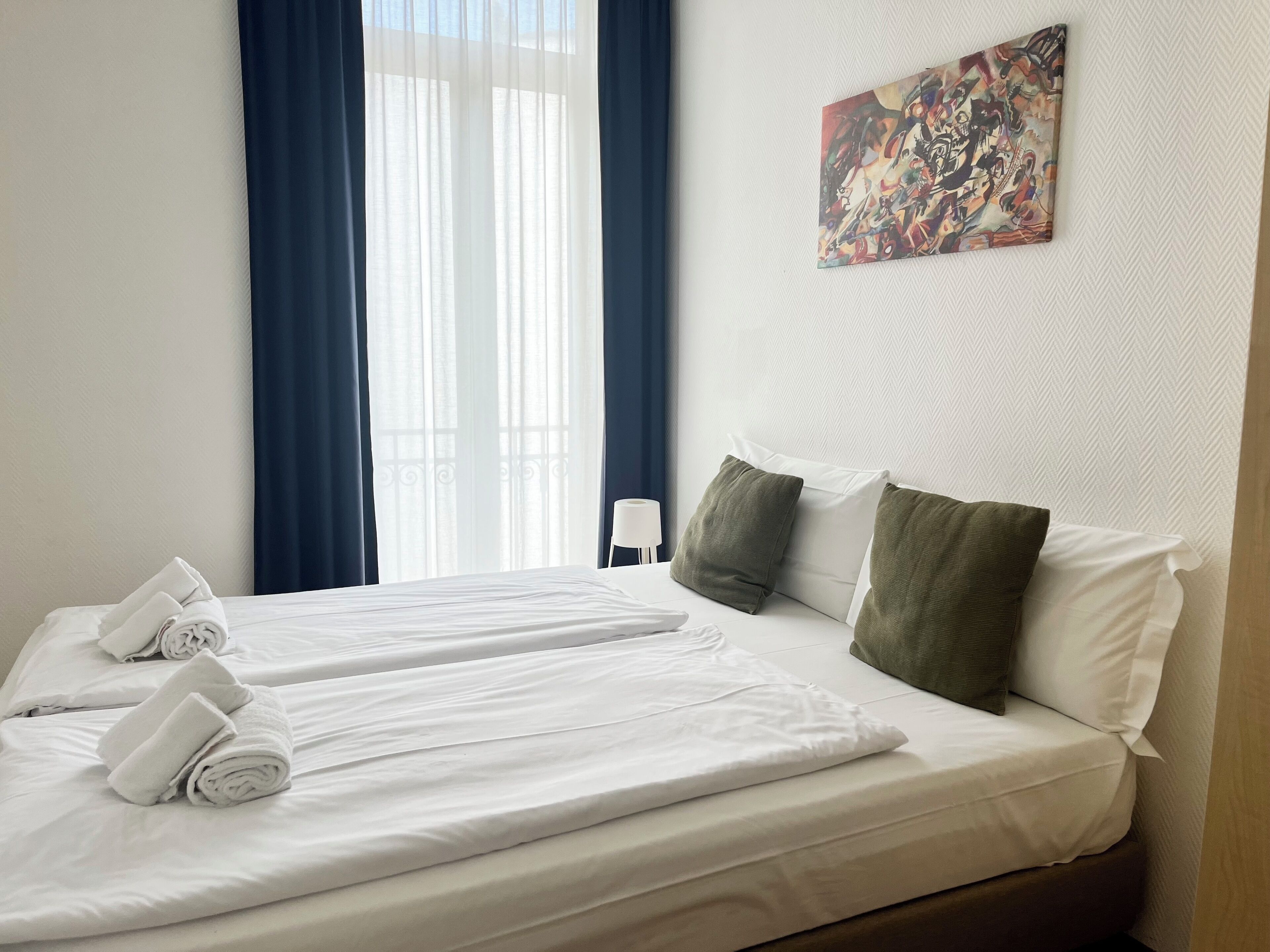 Una habitación de hotel con dos camas, un cuadro en la pared y una ventana con cortinas.