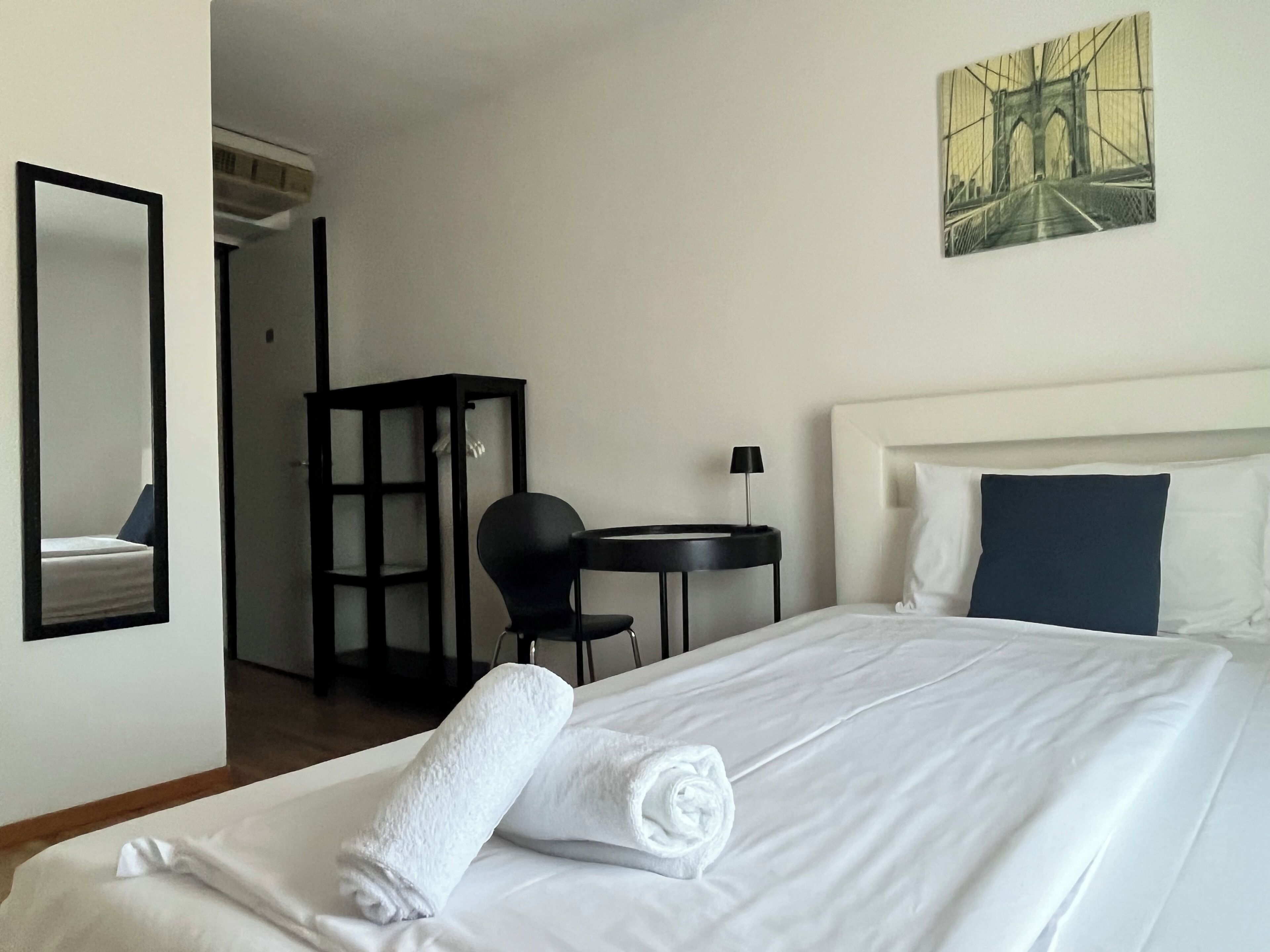 A hotel room with a bed, a desk, a chair, and a painting on the wall.