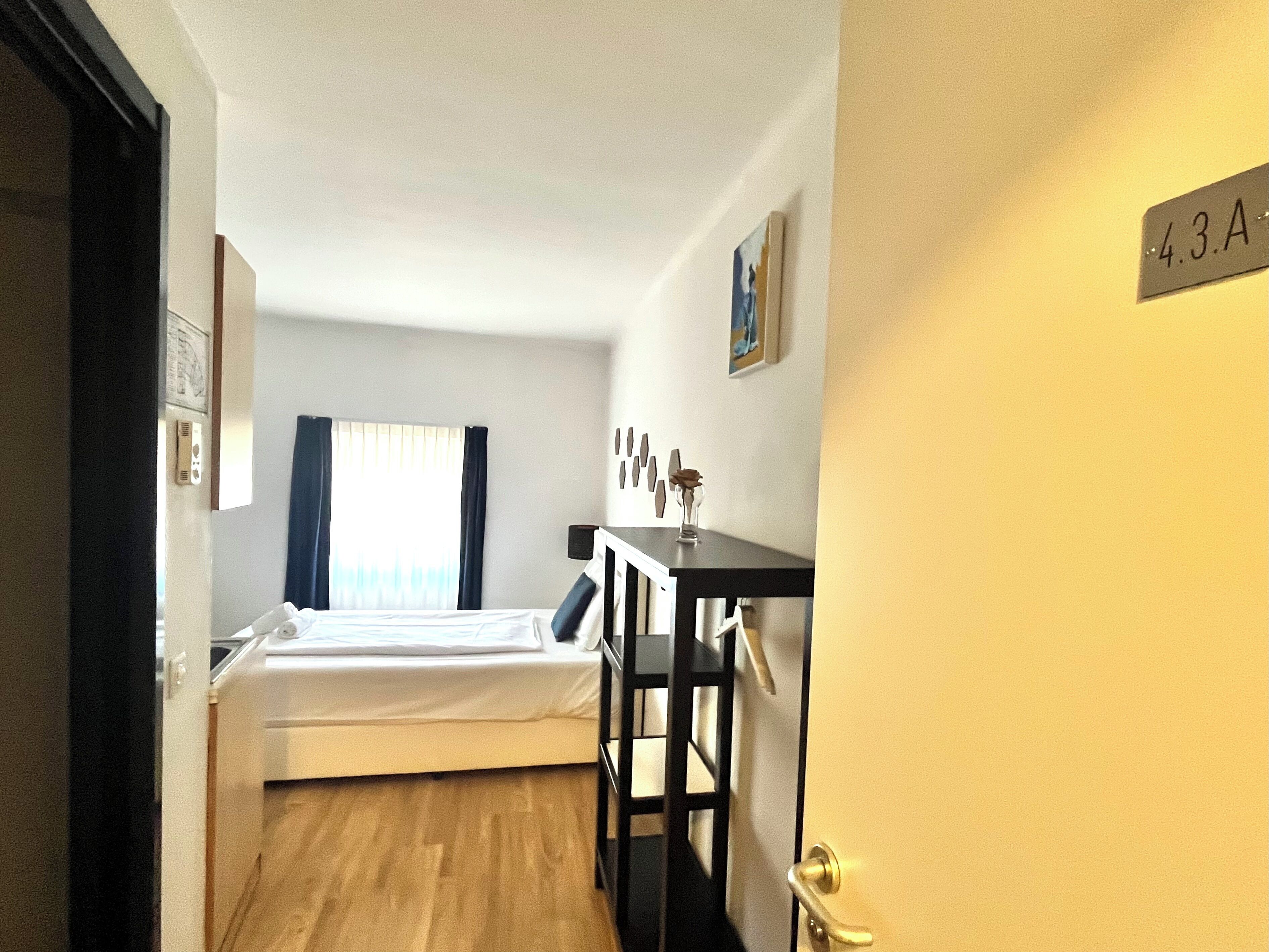 A hotel room with a bed, a desk, and a door marked with the number 43A.