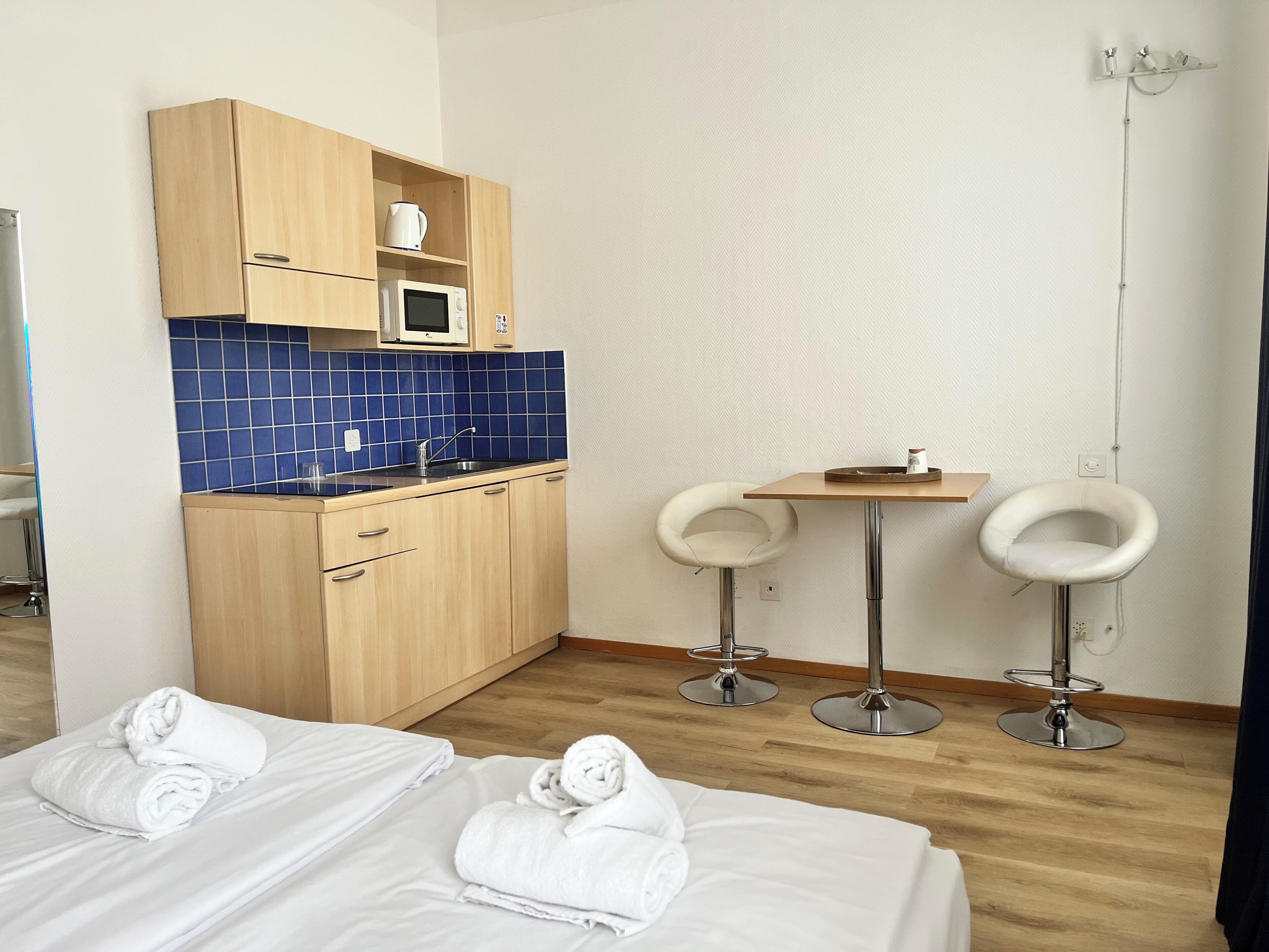 Et hotelværelse med en seng, et lille tekøkken, to hvide stole og et badeværelse.